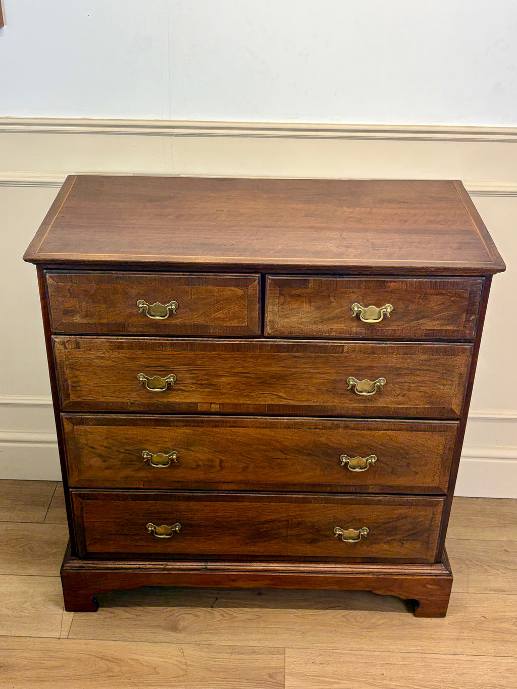 Wooden dresser with four drawers and brass handles on a wooden floor.