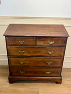 Wooden dresser with four drawers and brass handles on a wooden floor.