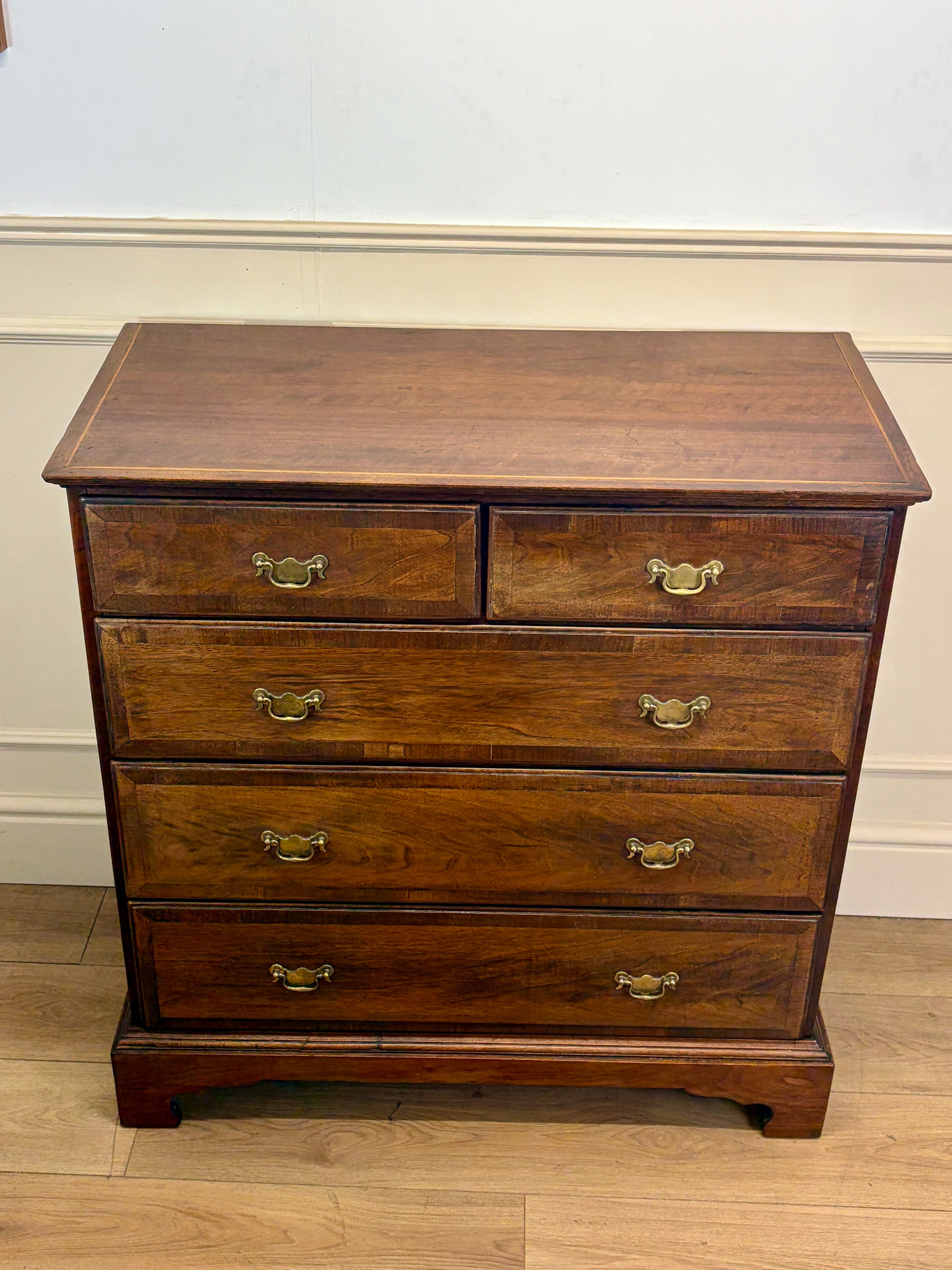 Wooden dresser with four drawers and brass handles on a wooden floor.