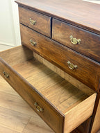 Wooden dresser with multiple drawers and brass handles on a wooden floor.