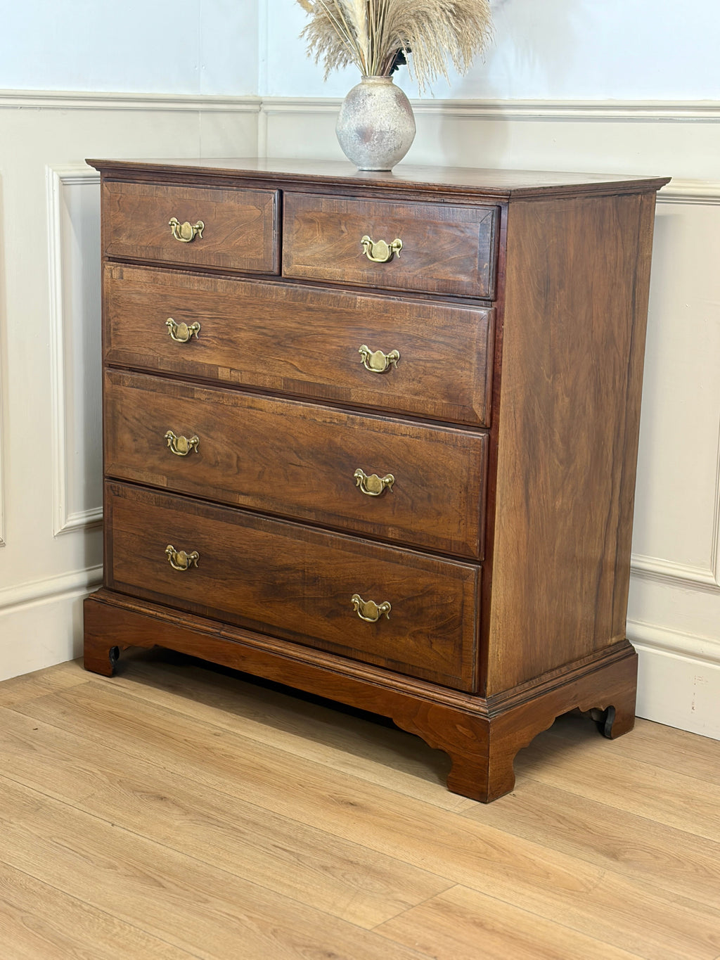 Wooden dresser with four drawers on a wooden floor against a white wall.