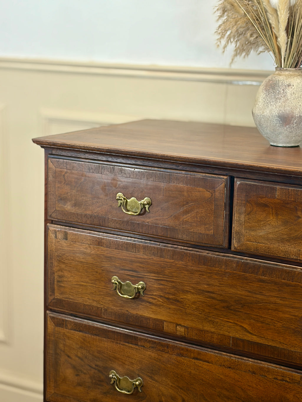 Wooden dresser with three drawers and a decorative vase on top against a light wall.