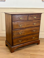 Wooden dresser with four drawers on a wooden floor against a white wall.