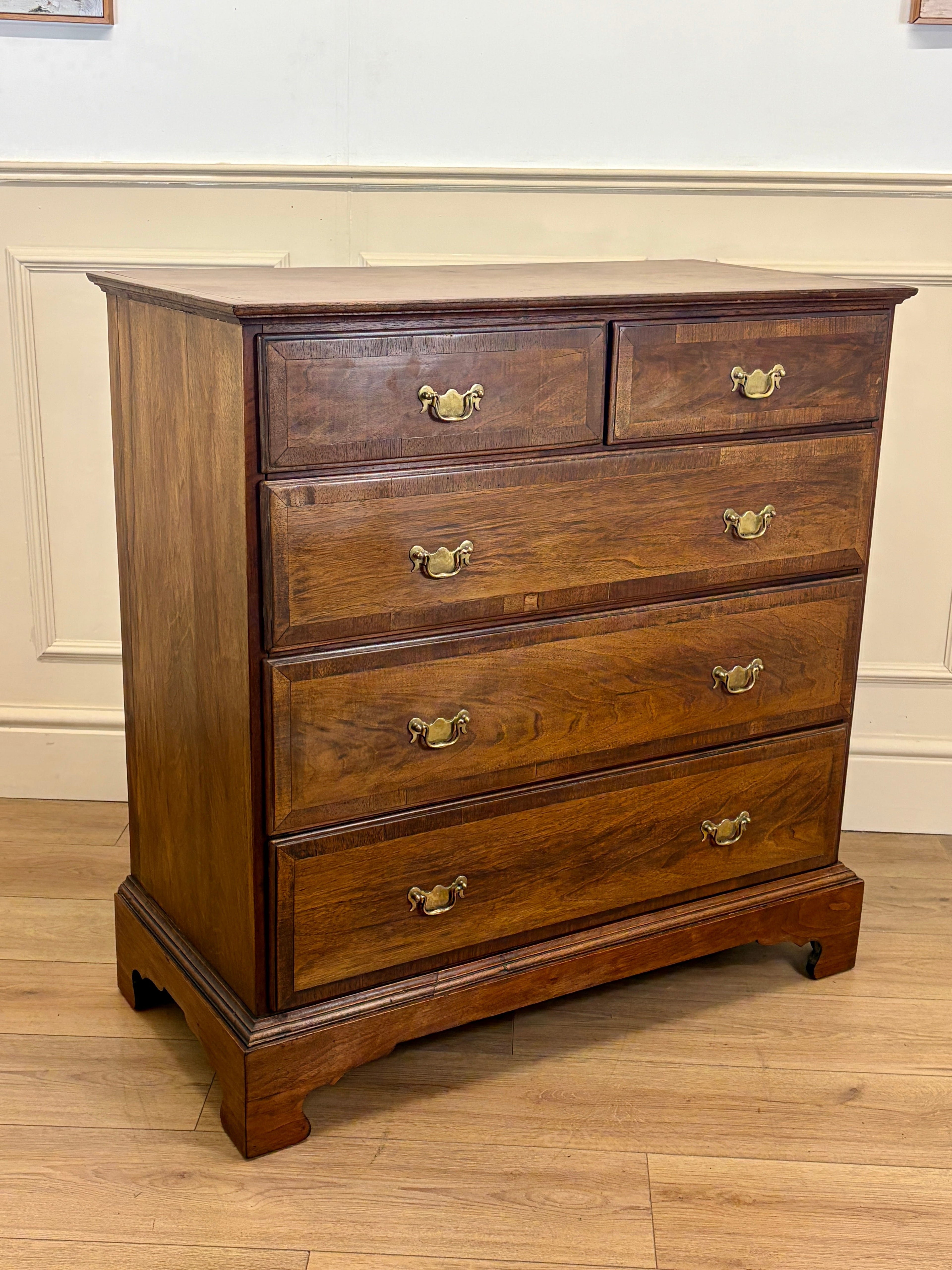 Wooden dresser with four drawers on a wooden floor against a white wall.