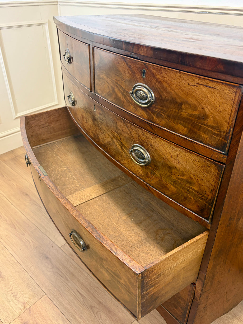 Wooden dresser with curved front and drawers on a wooden floor.