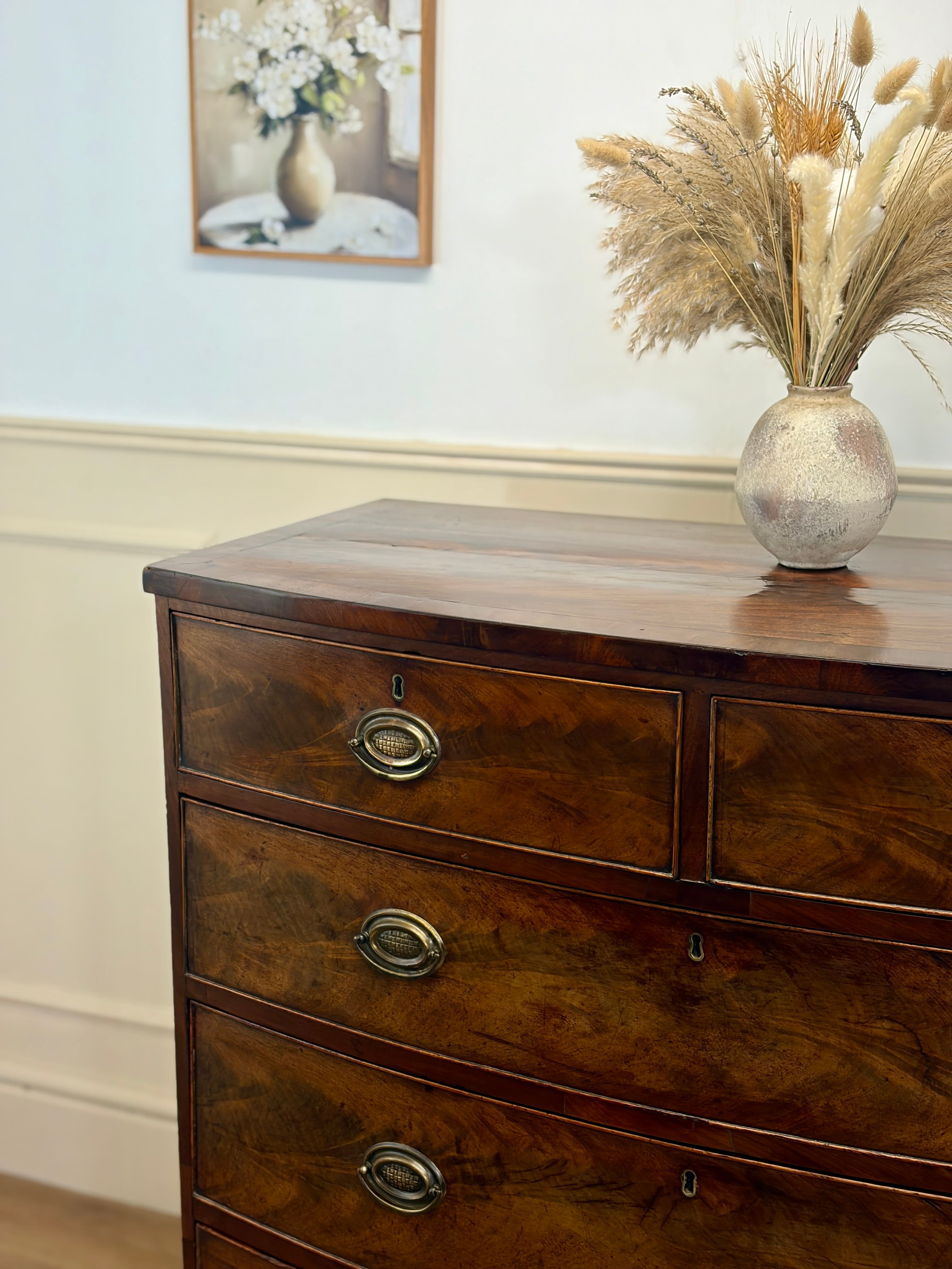 Wooden dresser with decorative vase and pampas grass against a light wall.