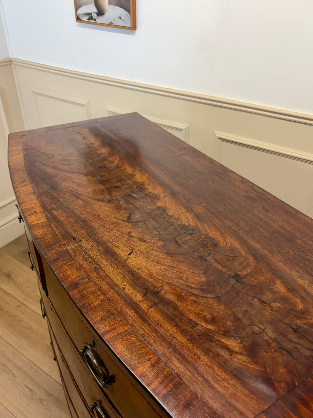 Wooden dresser with a curved top in a room with white walls and wooden floor.