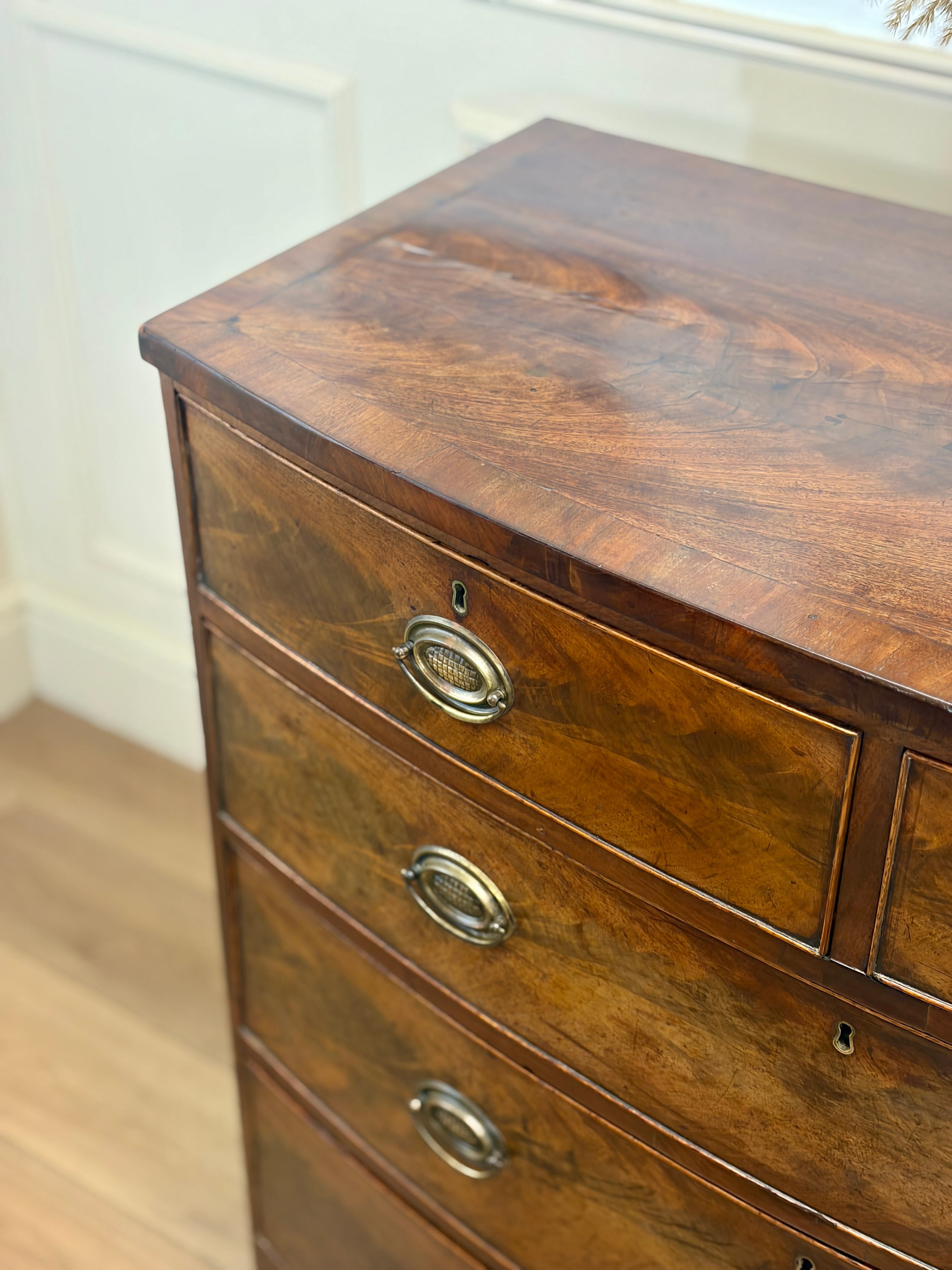 Wooden dresser with curved top and brass handles on a wooden floor.