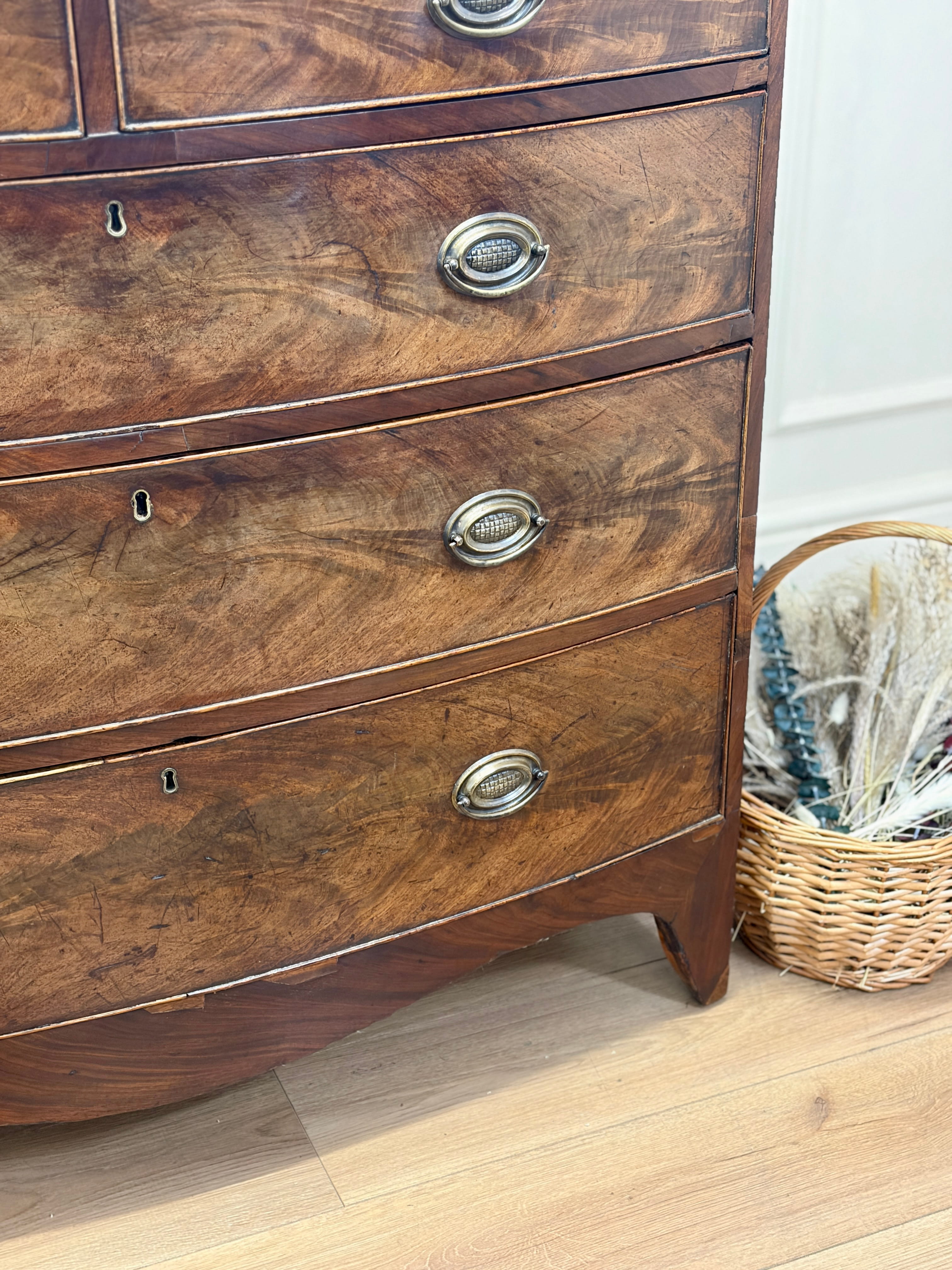 Wooden dresser with metal handles on a wooden floor, with a basket in the background.