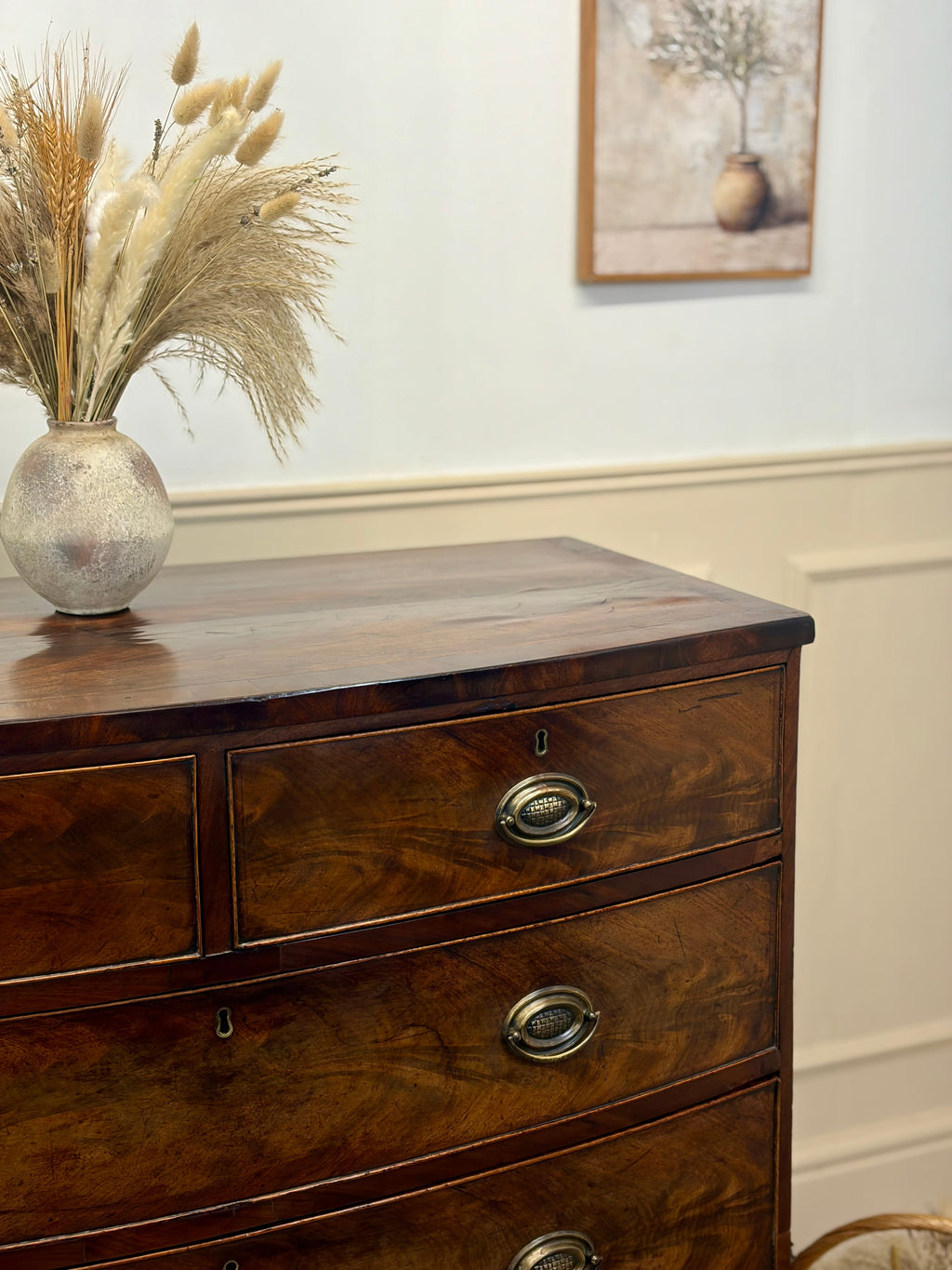 Wooden dresser with decorative vase and dried plants against a neutral wall.