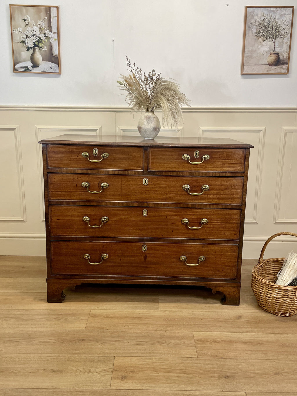Wooden dresser with four drawers in a room with framed pictures on the wall.