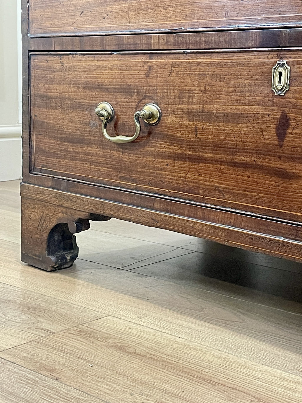 Close-up of a wooden dresser with brass handle and lock on a wooden floor.