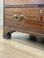 Close-up of a wooden dresser with brass handle and lock on a wooden floor.
