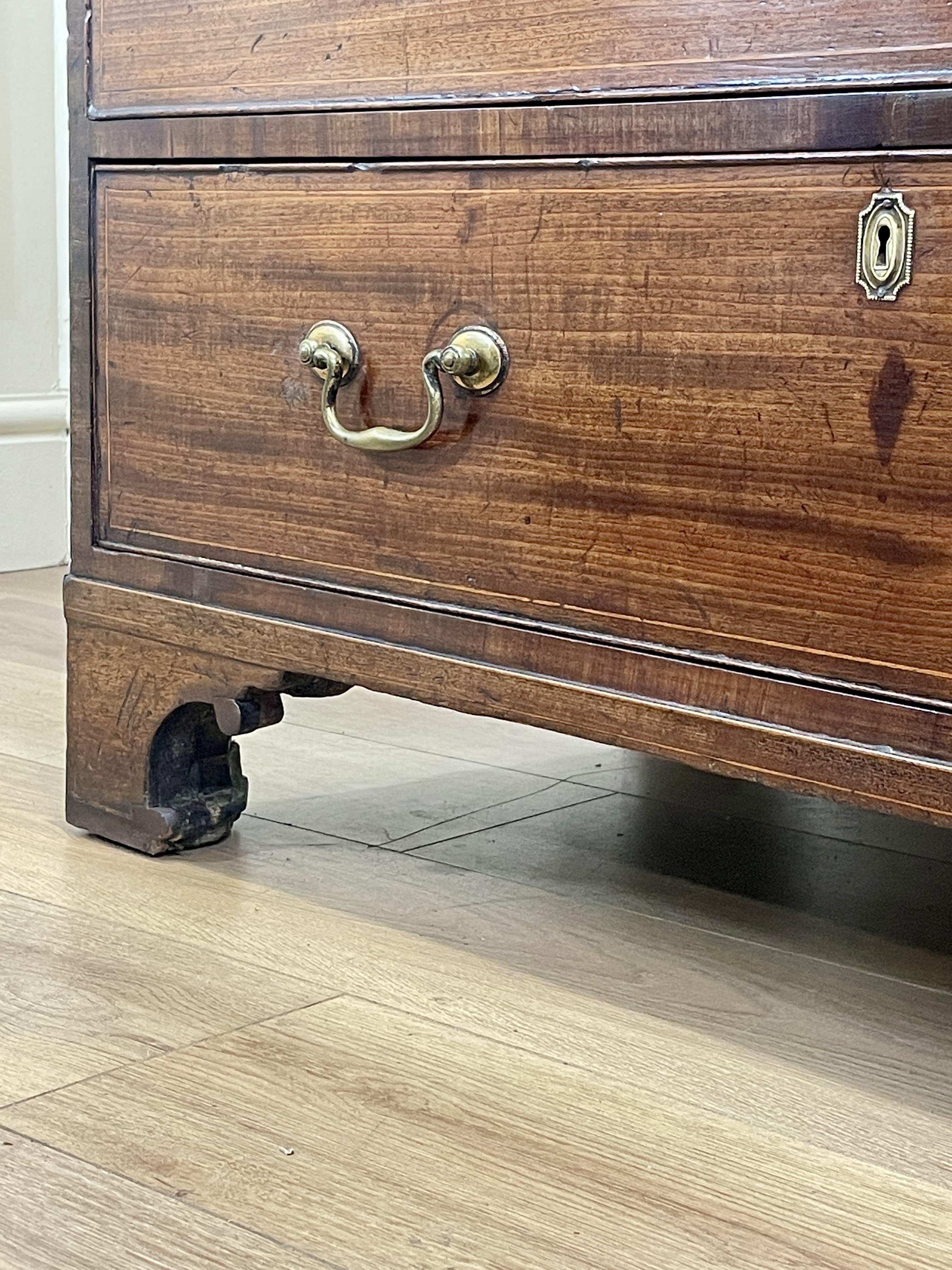 Close-up of a wooden dresser with brass handle and lock on a wooden floor.