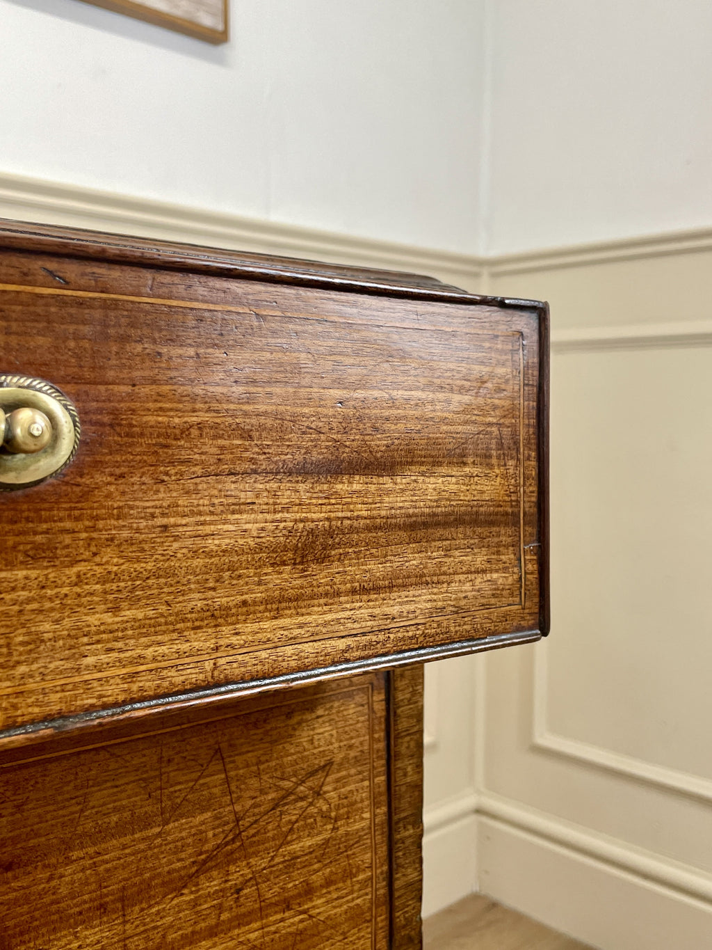 Close-up of a wooden piece of furniture with a brass handle against a neutral wall.