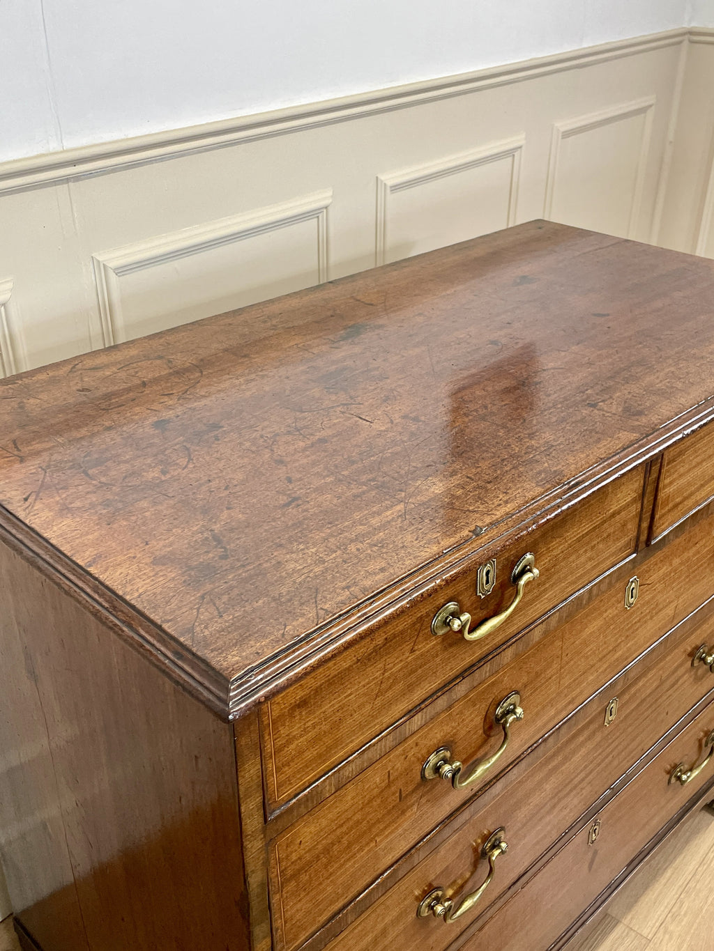 Wooden dresser with brass handles against a white paneled wall.