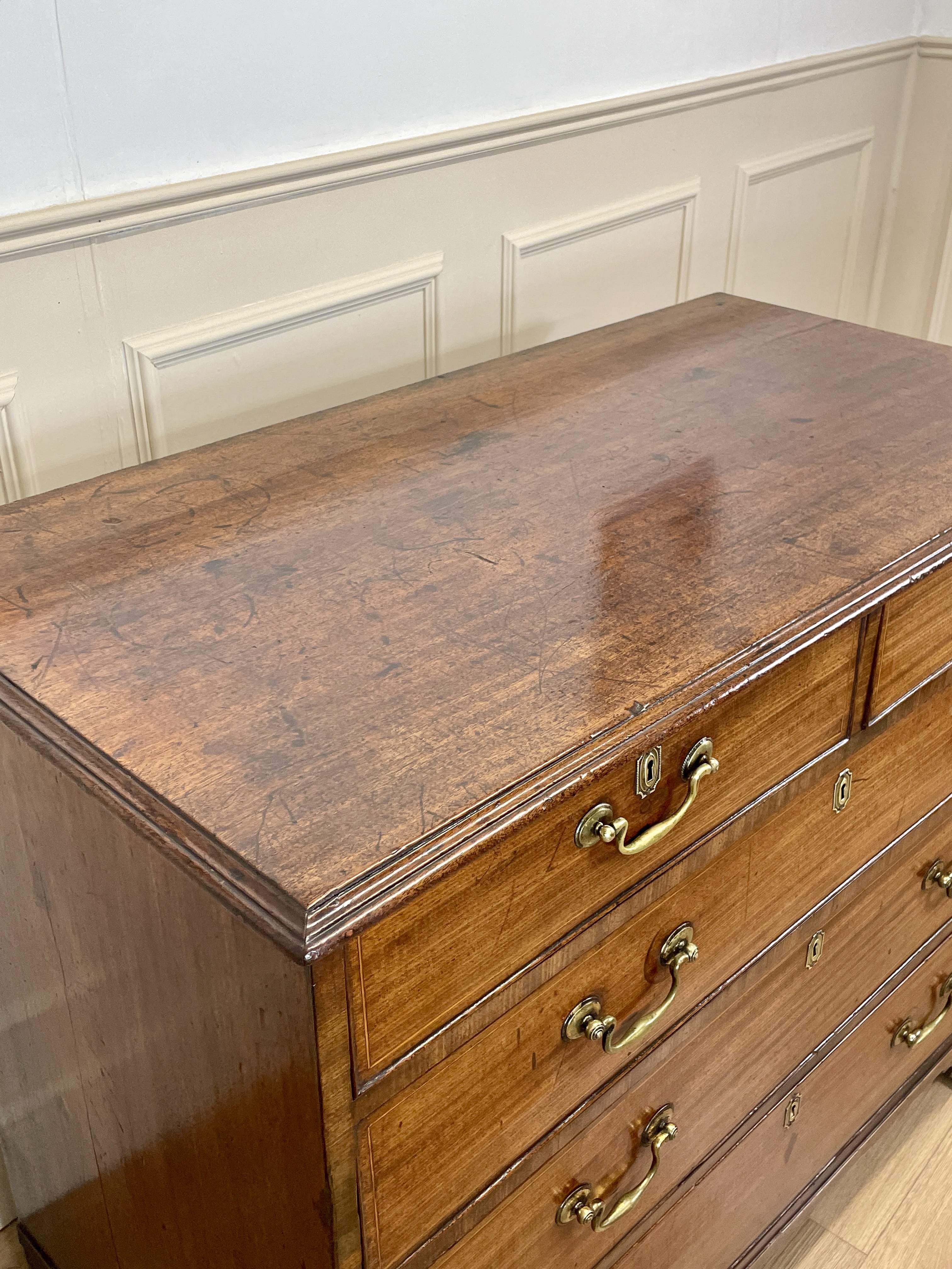 Wooden dresser with brass handles against a white paneled wall.