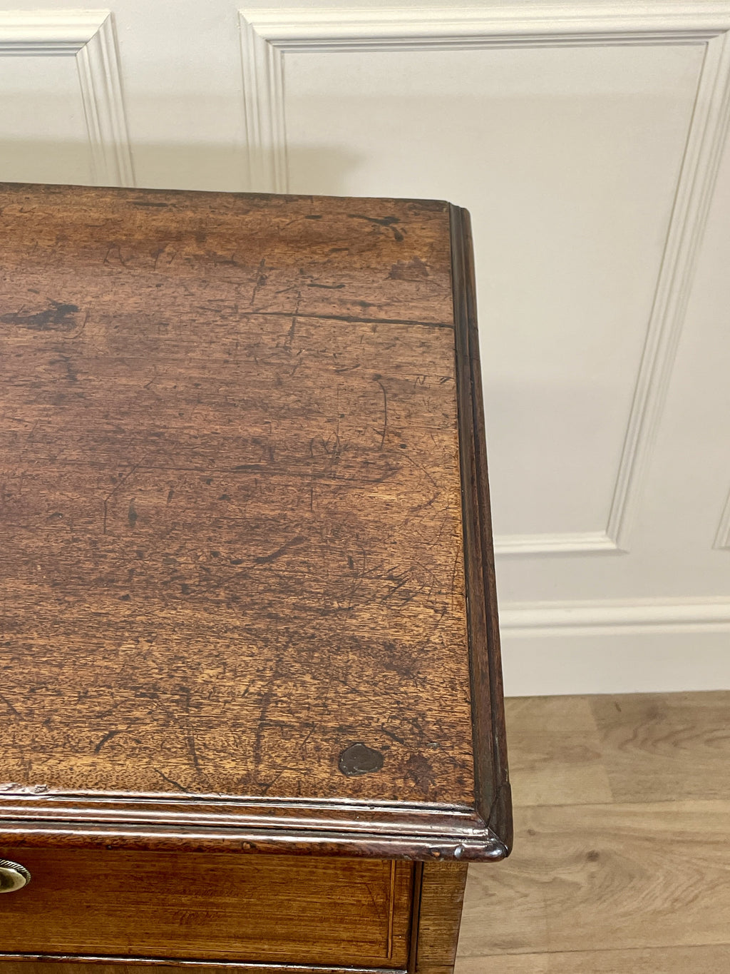 Wooden side table with a worn surface against a white paneled wall.