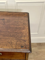 Wooden side table with a worn surface against a white paneled wall.