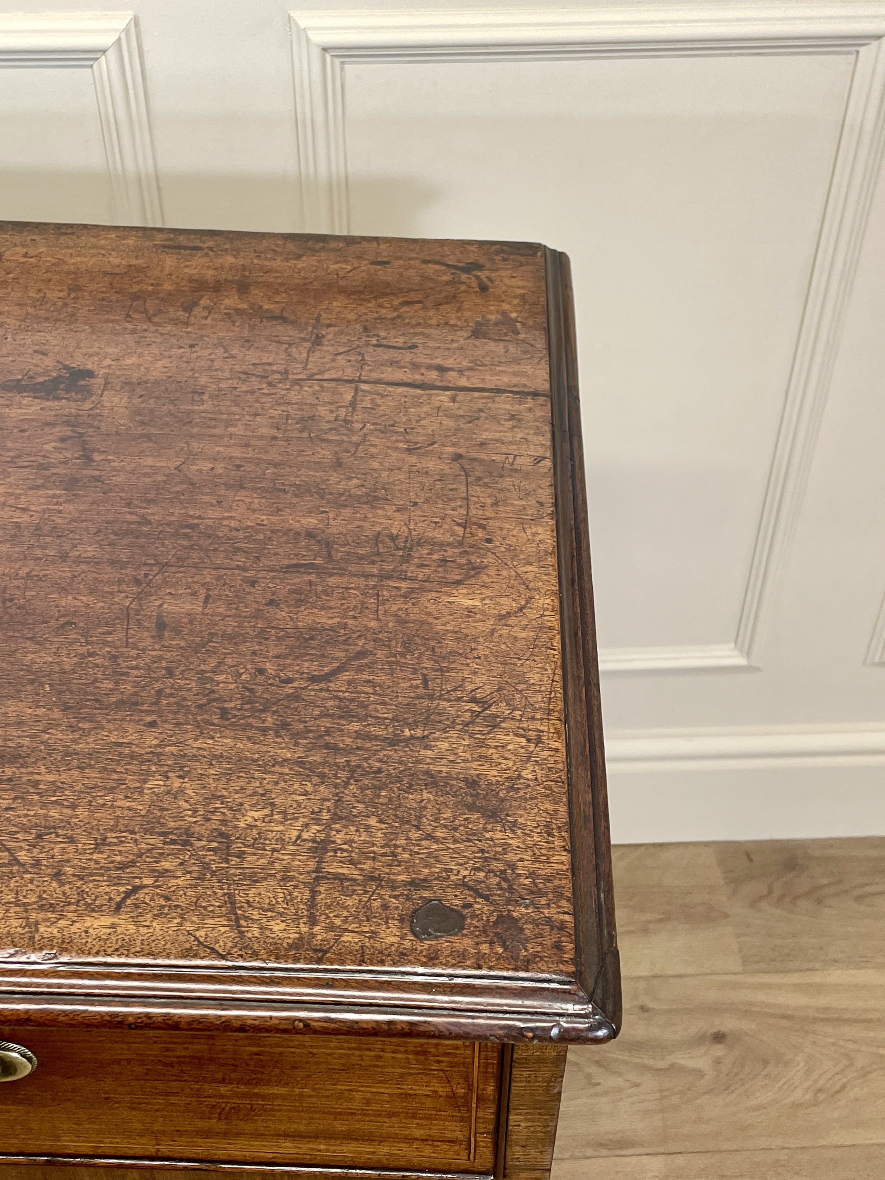 Wooden side table with a worn surface against a white paneled wall.