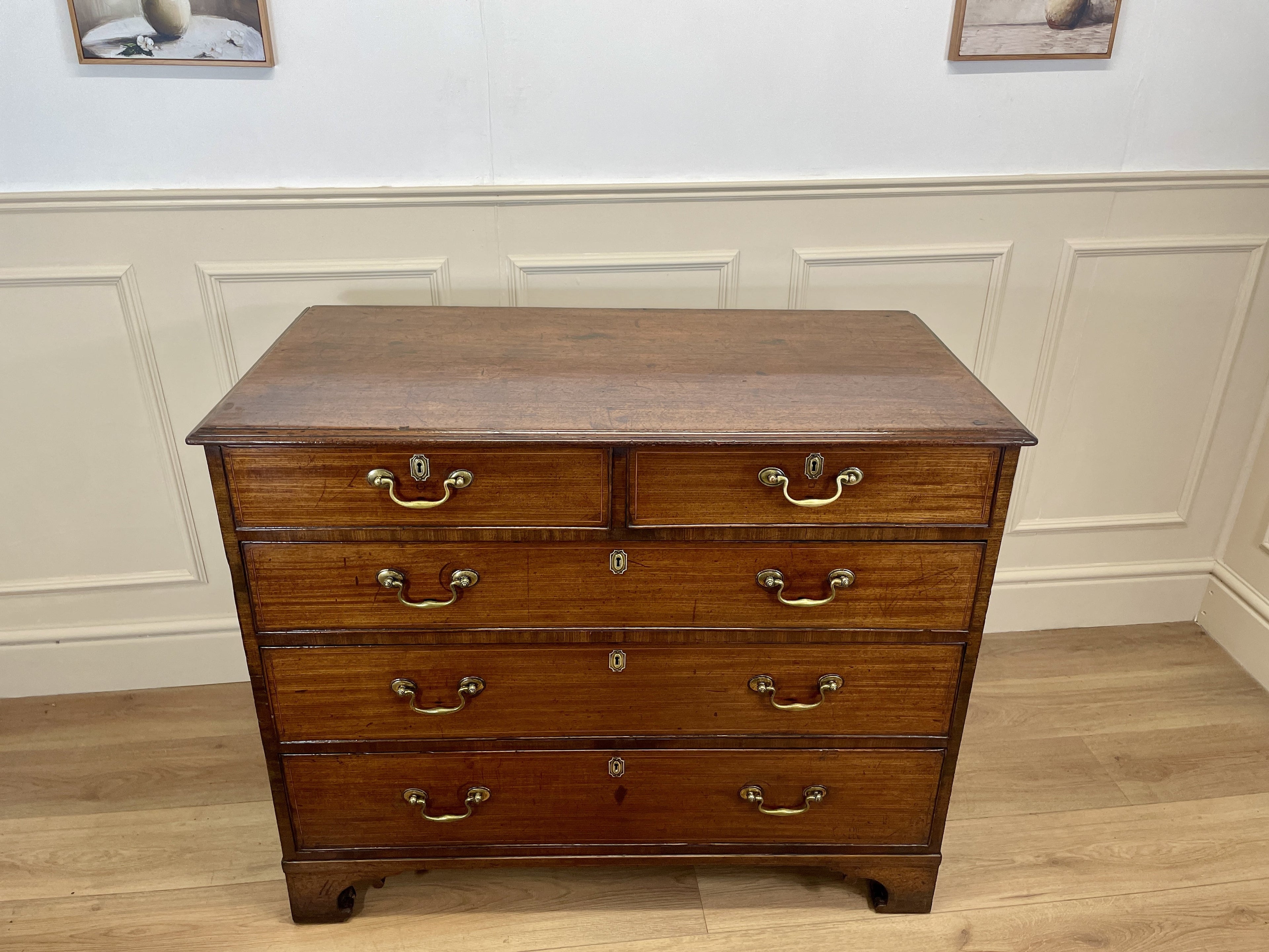 Wooden dresser with multiple drawers on a wooden floor against a white paneled wall.