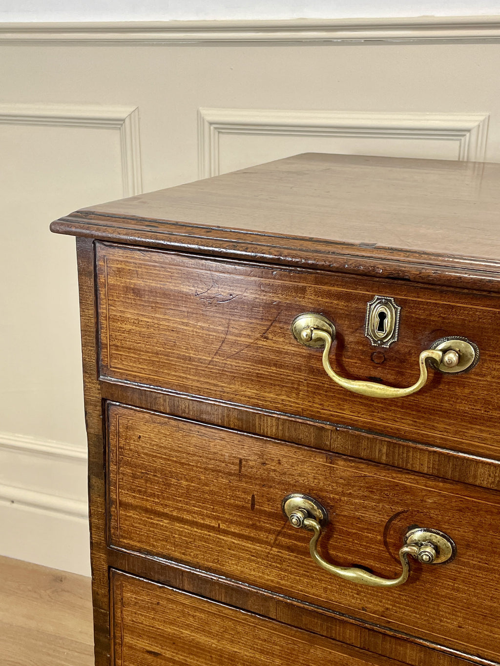 Wooden dresser with brass handles against a beige wall.