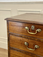 Wooden dresser with brass handles against a beige wall.