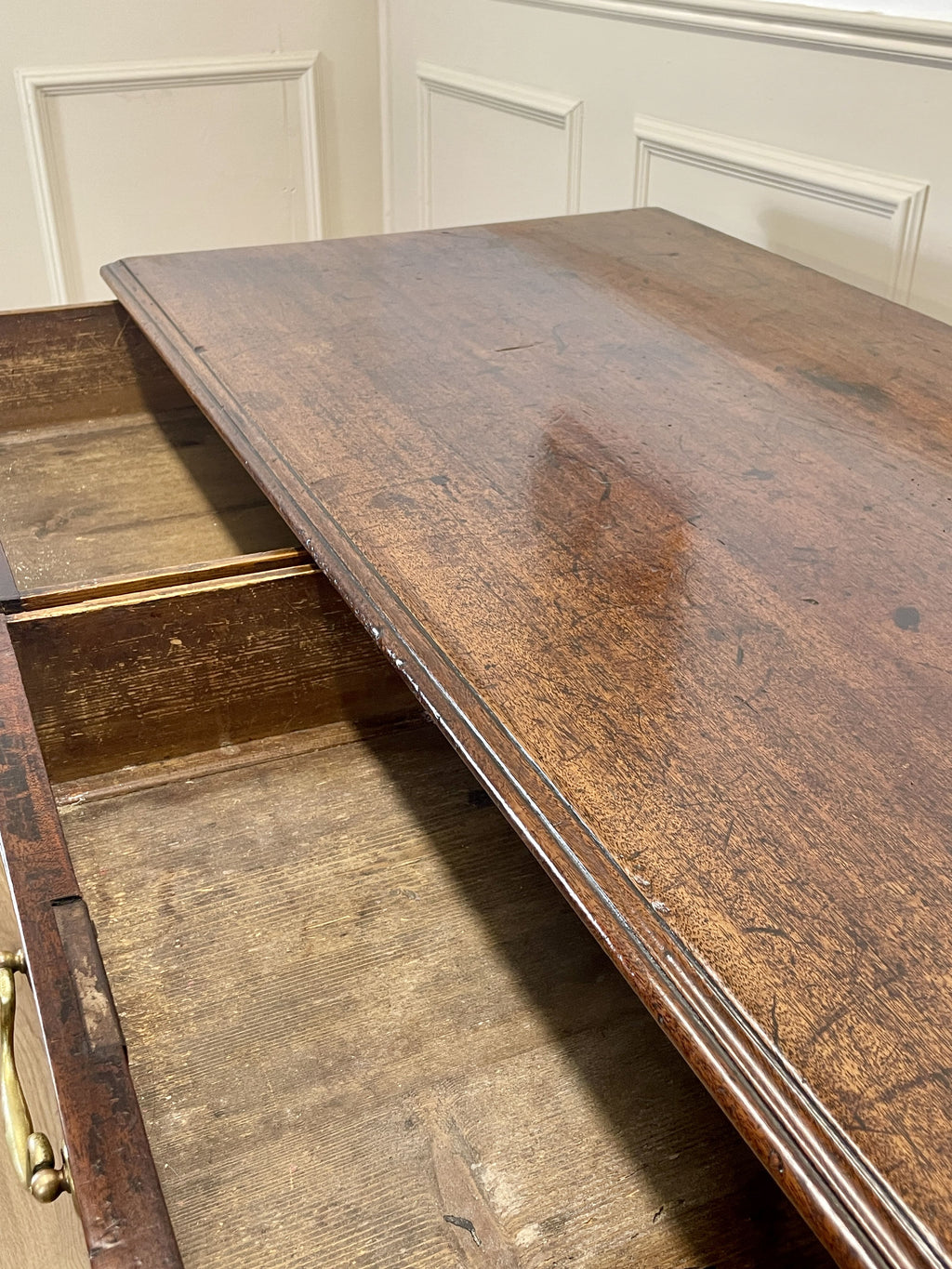 Wooden desk with a visible drawer in a room with white paneled walls.