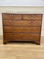 Wooden dresser with multiple drawers and brass handles on a wooden floor.
