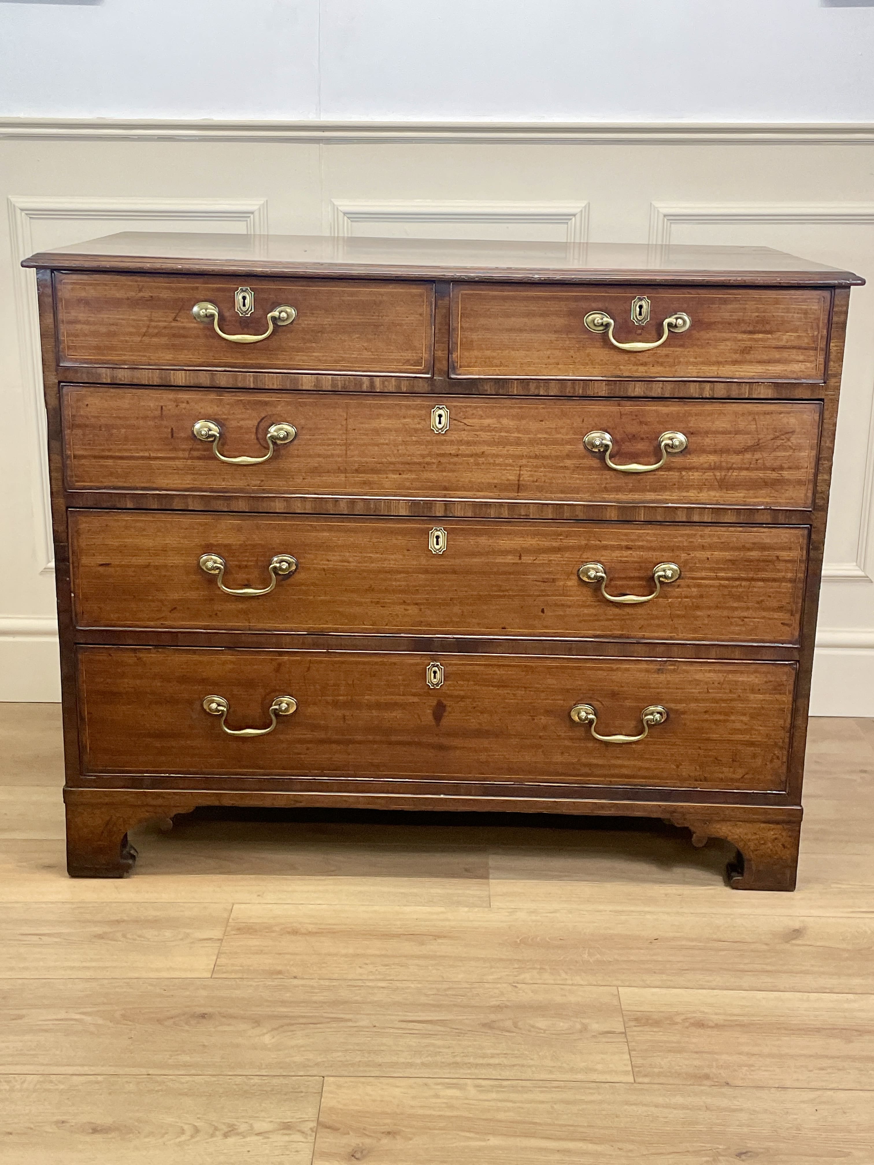 Wooden dresser with multiple drawers and brass handles on a wooden floor.