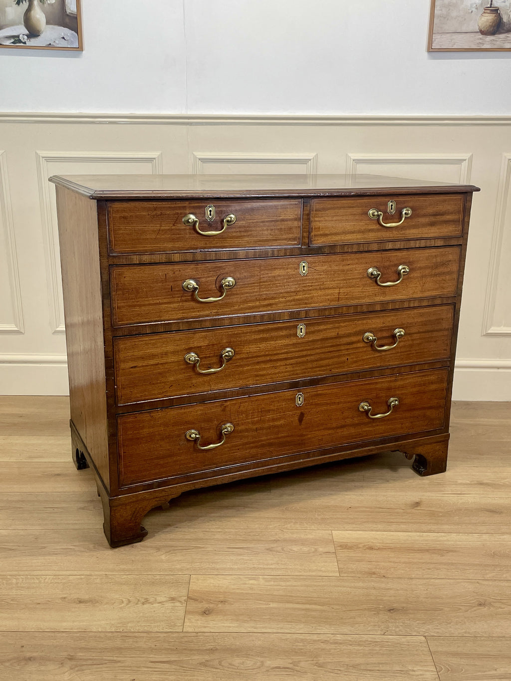 Wooden dresser with multiple drawers and brass handles on a wooden floor.