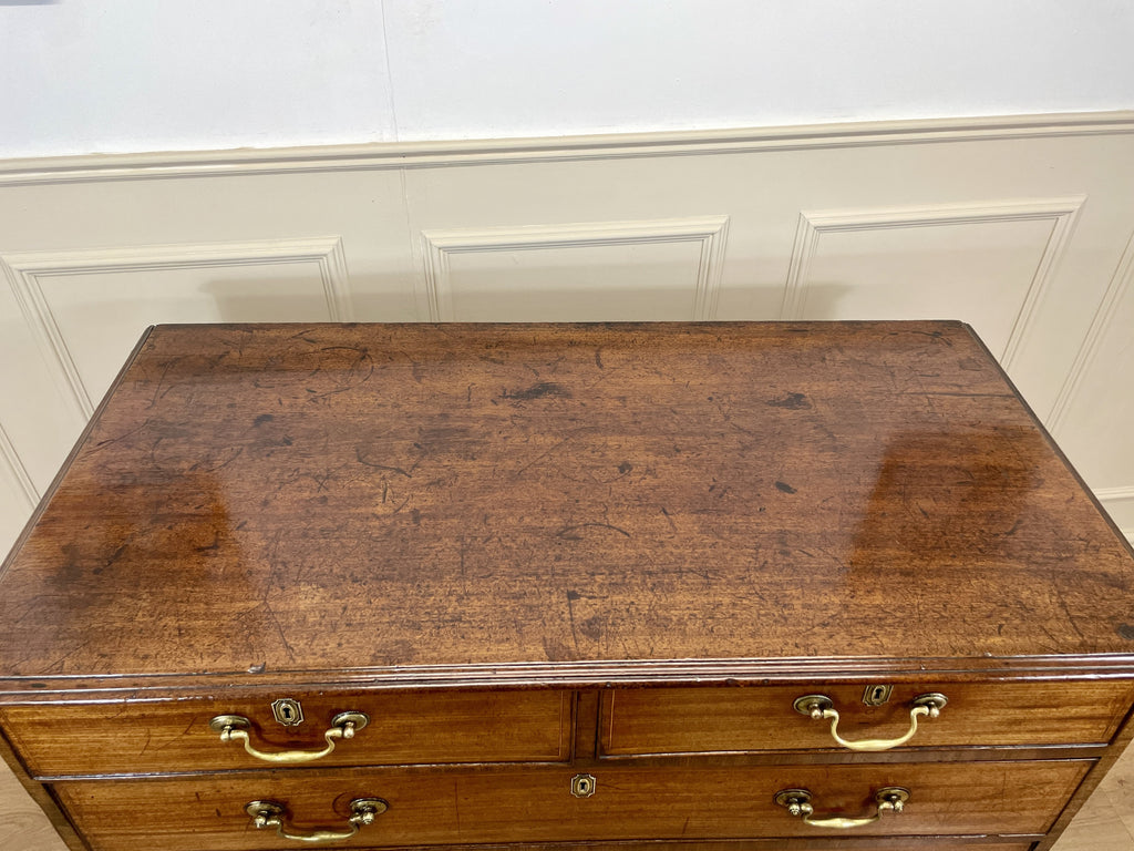 Vintage wooden dresser with brass handles against a white paneled wall.
