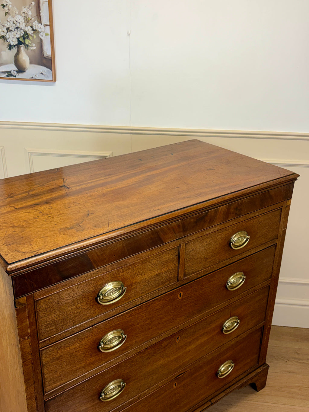 Wooden dresser with brass handles in a room with a painting on the wall.