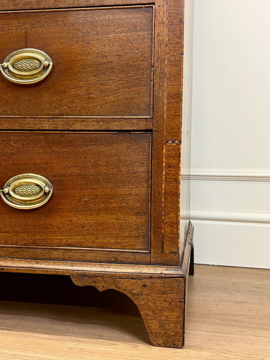 Wooden dresser with brass handles against a white wall.