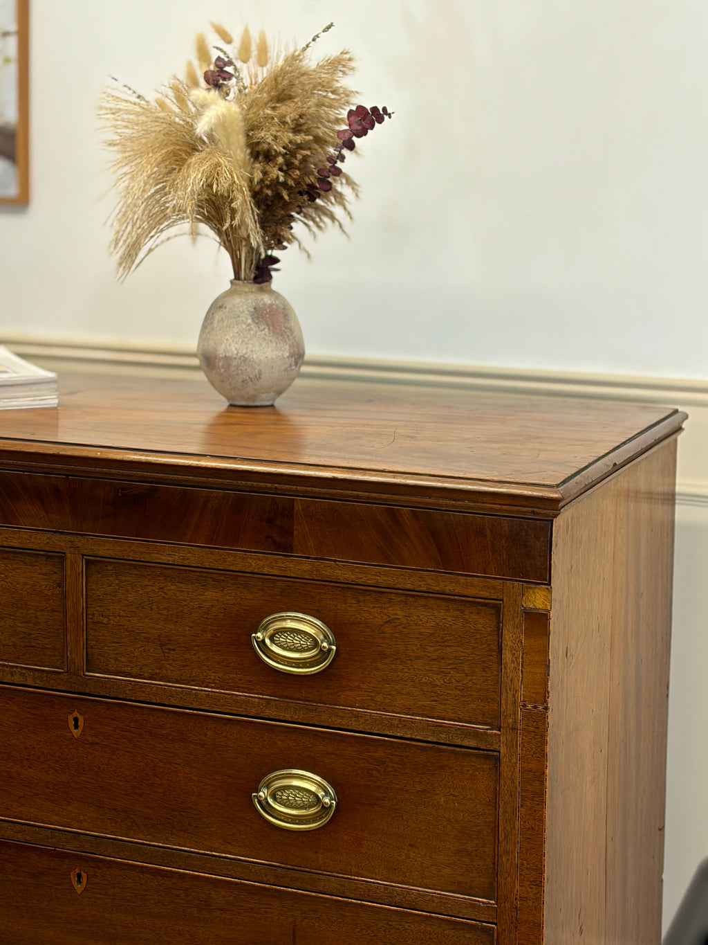 Wooden dresser with gold handles and a vase of dried flowers on top