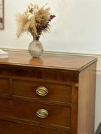 Wooden dresser with gold handles and a vase of dried flowers on top
