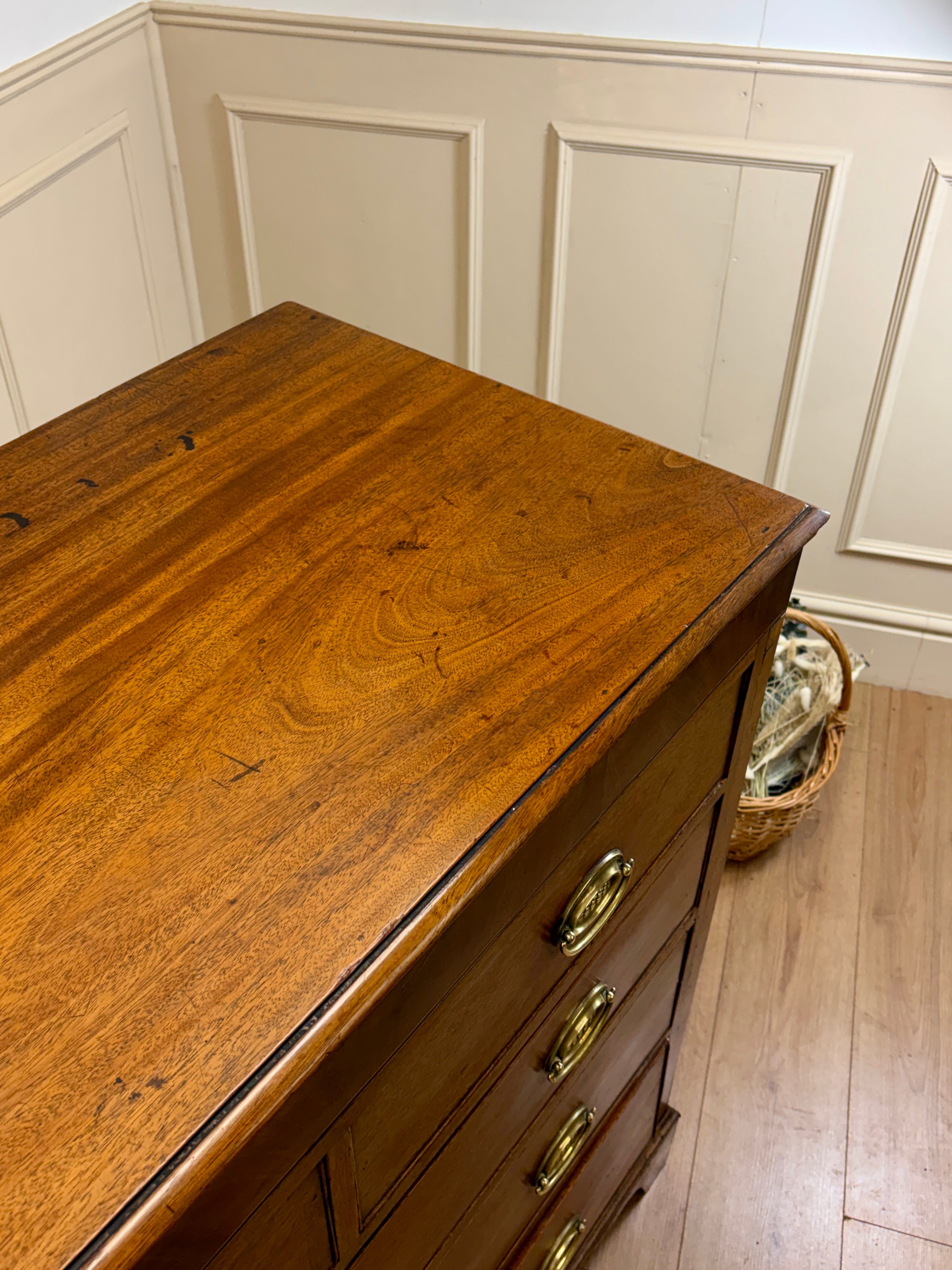 Wooden dresser with brass handles against a paneled wall.