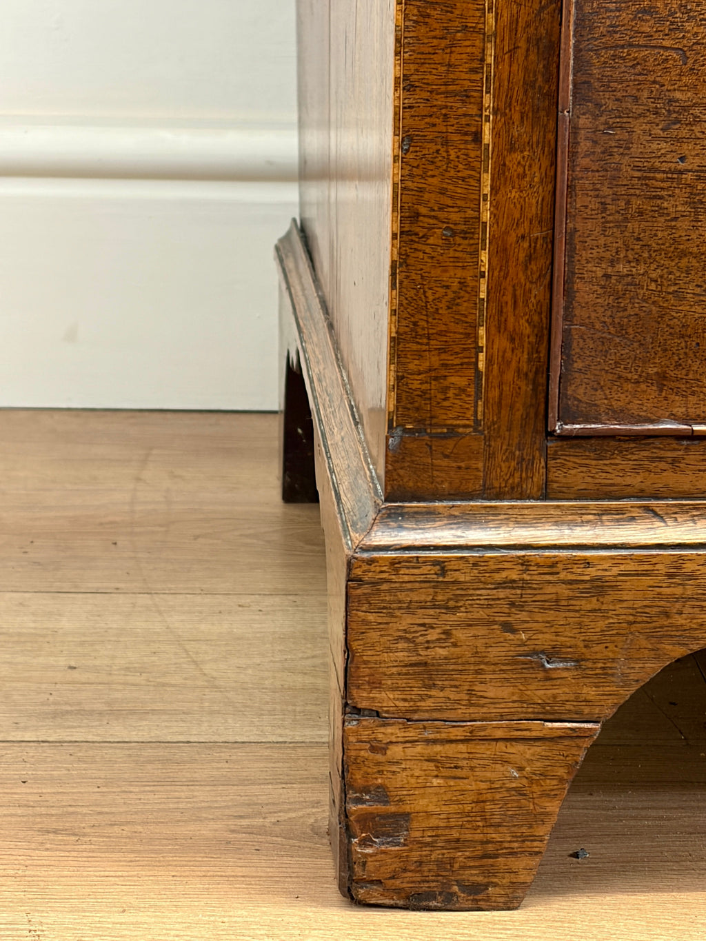 Close-up of a wooden cabinet corner with a white baseboard in the background