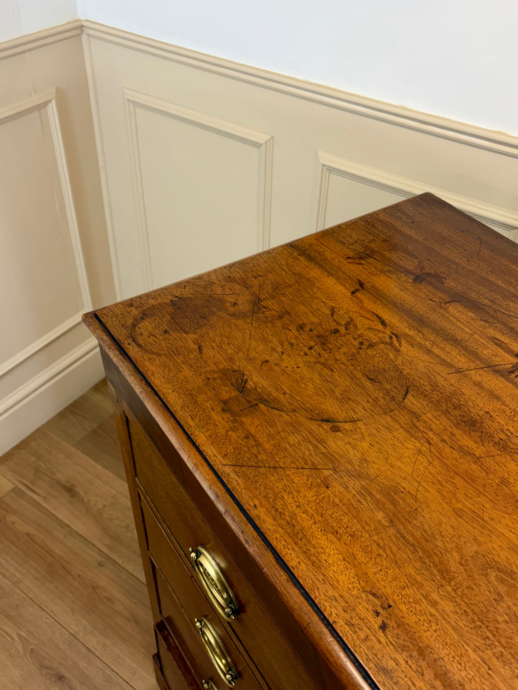 Wooden dresser with a gold handle against a white paneled wall.