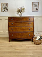 Wooden dresser with decorative items on a wooden floor and white wall.