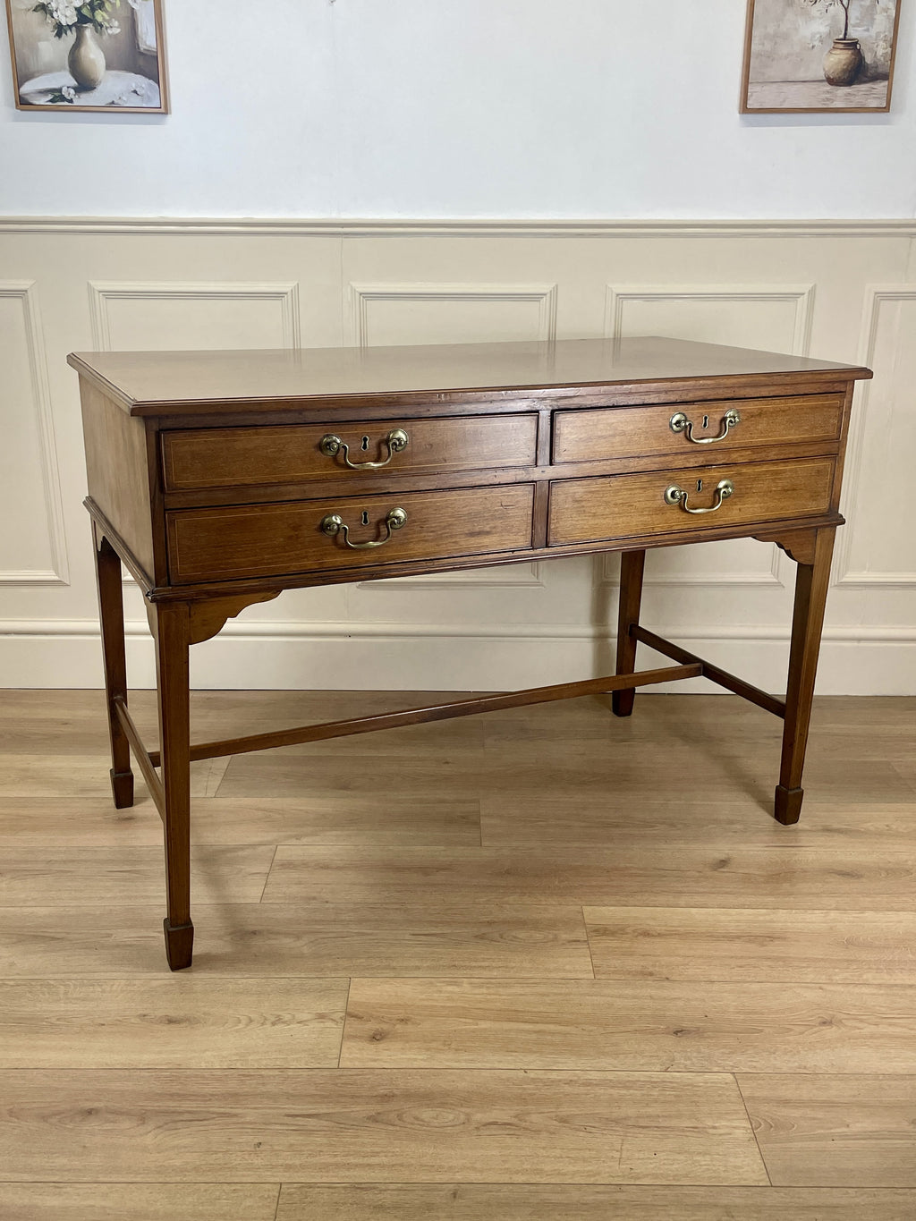 Wooden desk with drawers on a wooden floor against a white paneled wall.