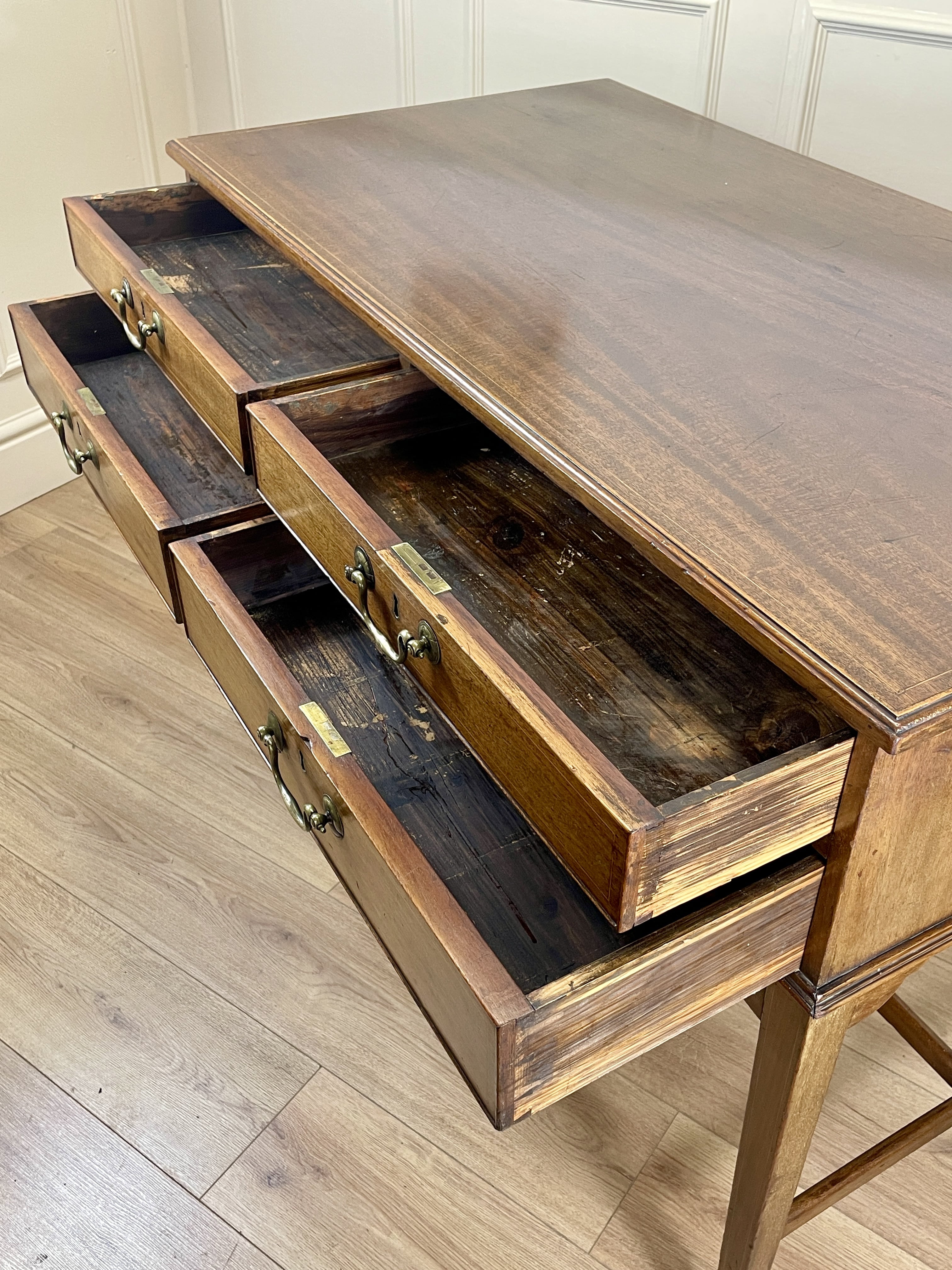 Wooden desk with multiple drawers on a light wood floor.
