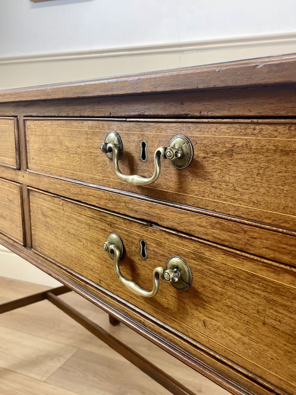 Wooden dresser with brass handles and keyholes on a light wooden floor.