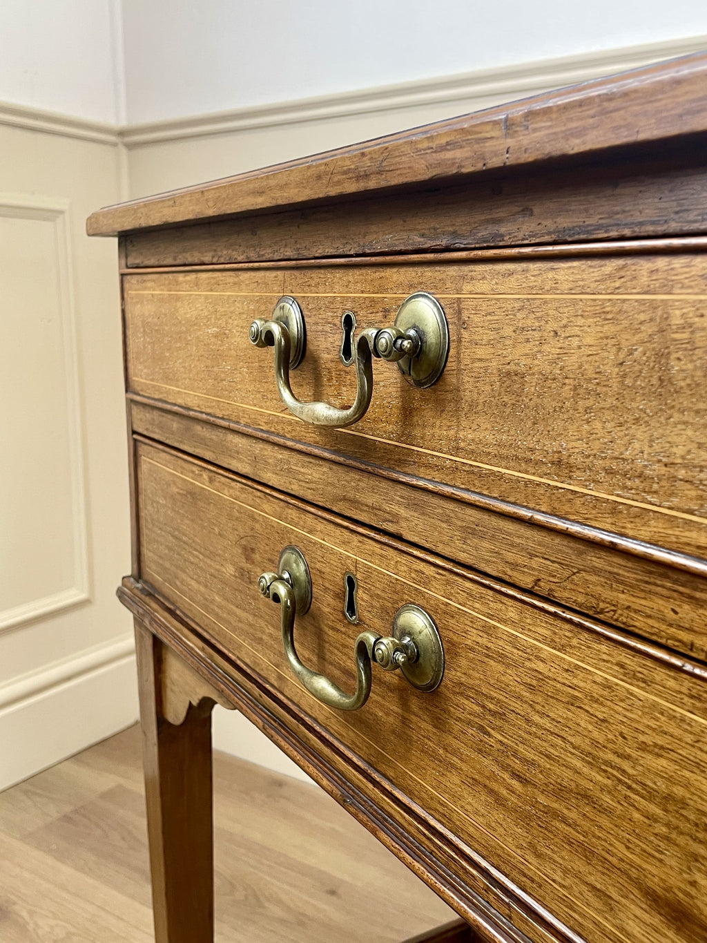 Wooden dresser with brass handles and locks against a white wall.