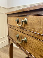 Wooden dresser with brass handles and locks against a white wall.