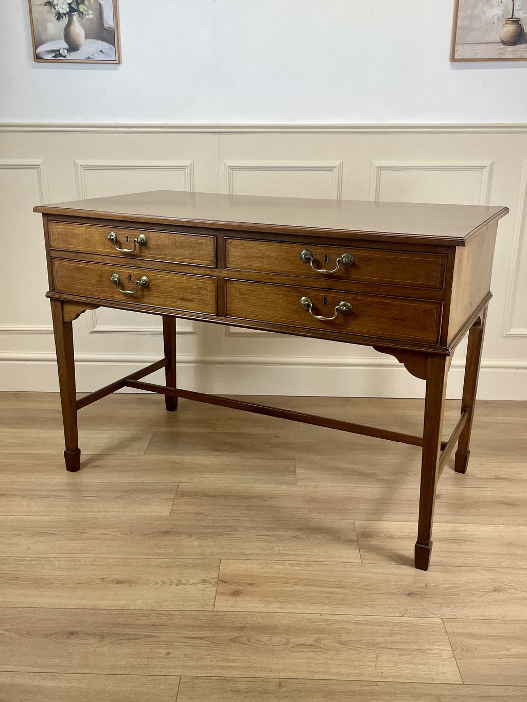 Wooden desk with three drawers on a wooden floor against a white wall.