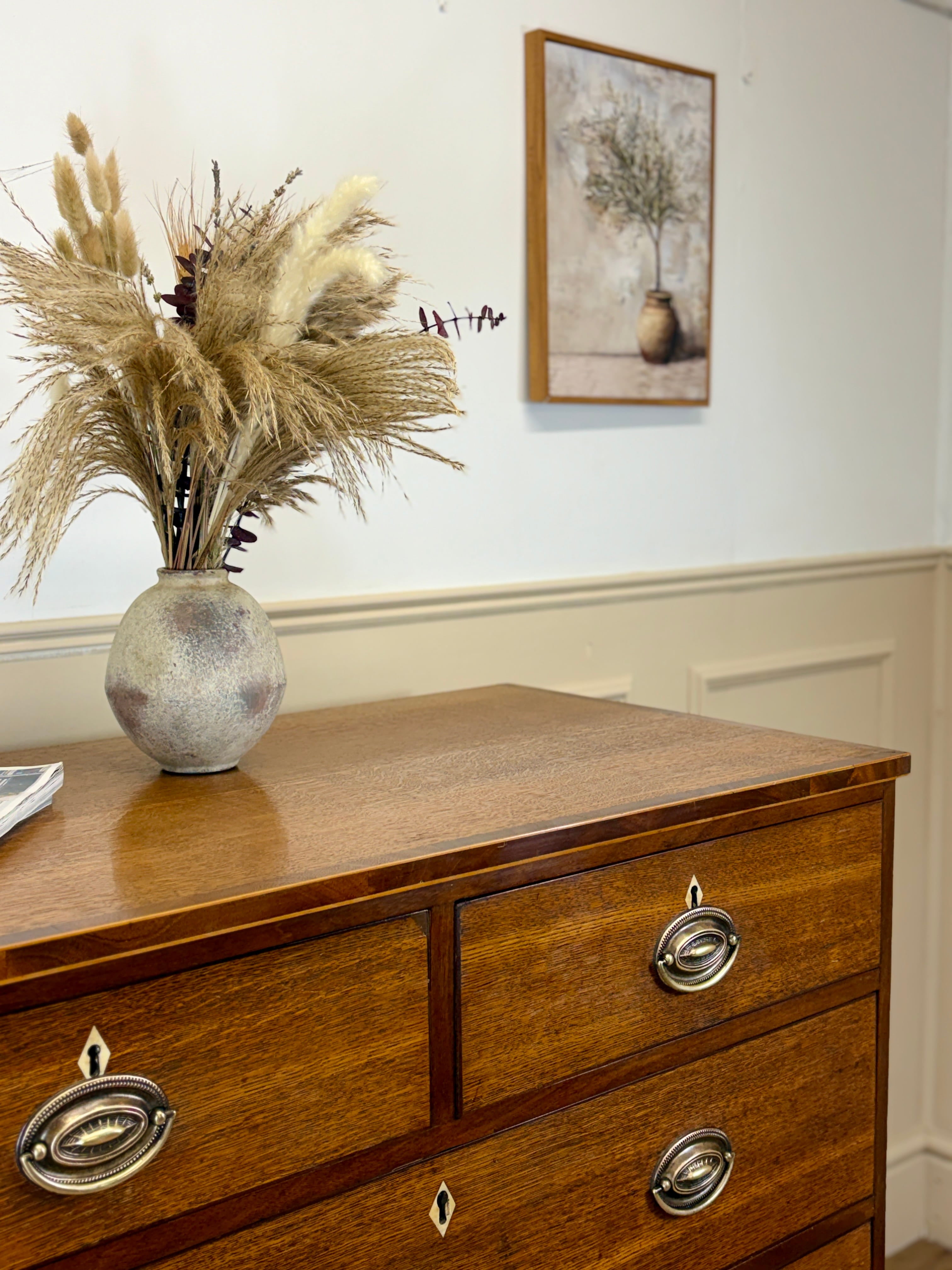Wooden dresser with decorative vase and pampas grass, framed picture on wall.