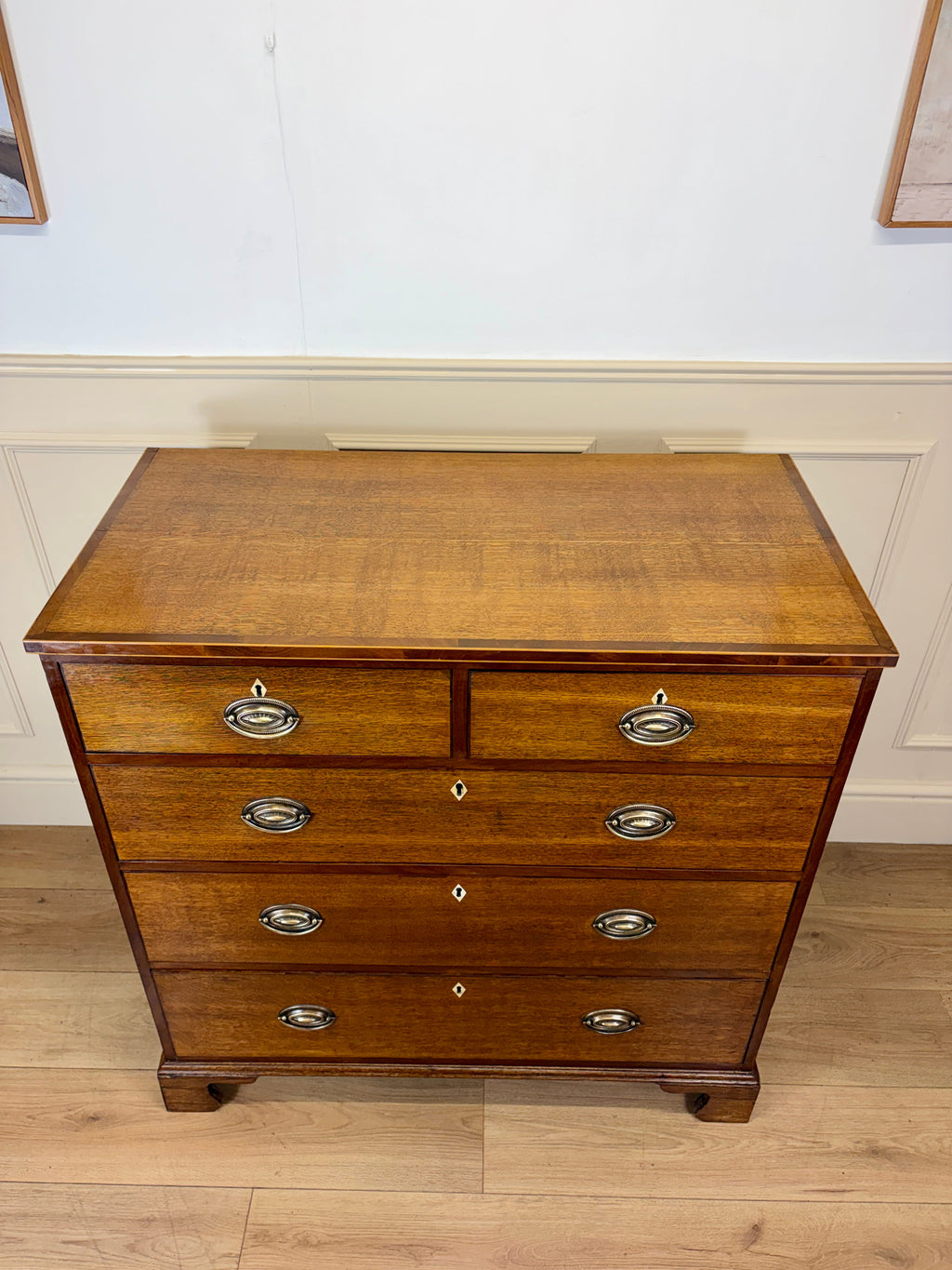 Wooden dresser with four drawers on a wooden floor against a white wall.