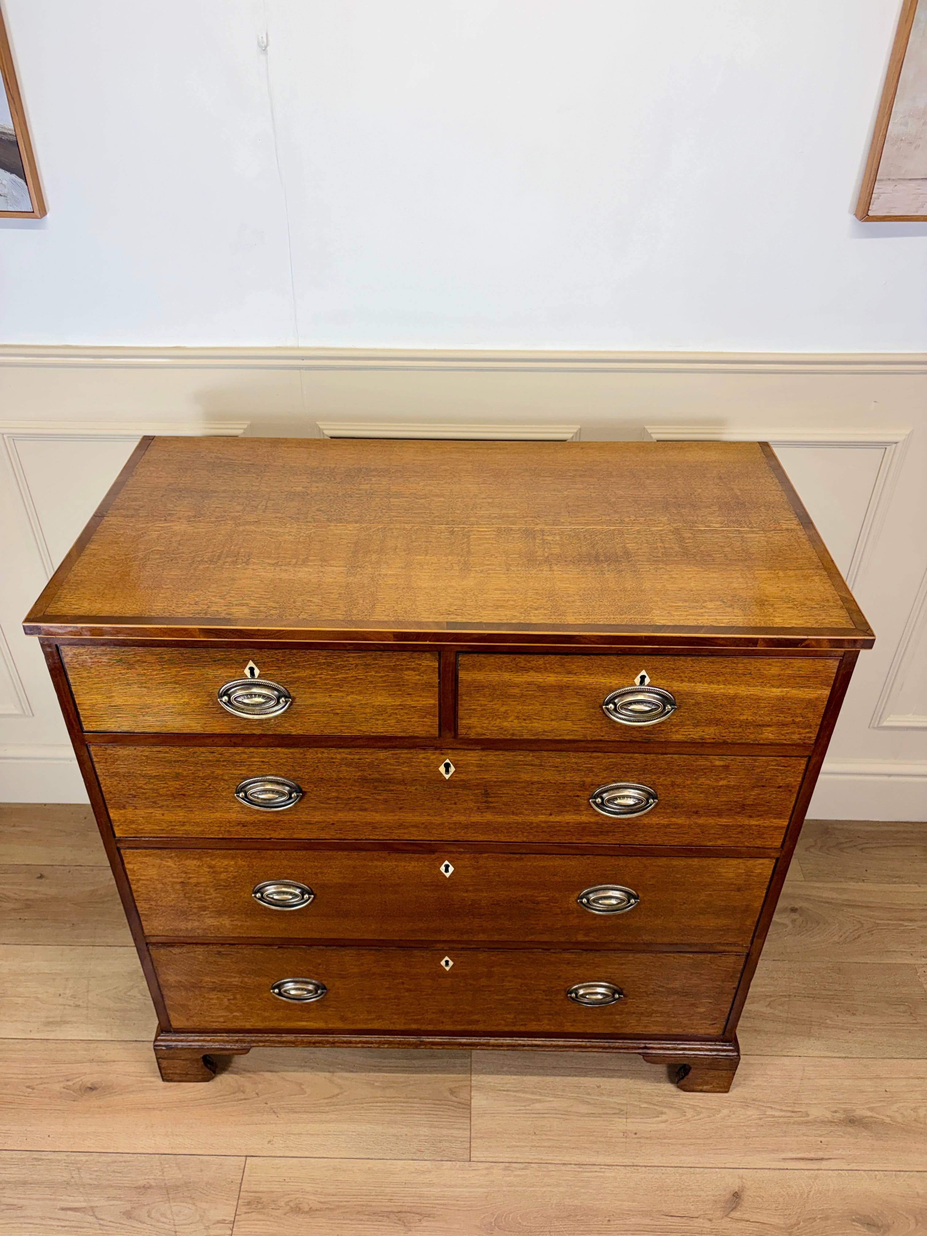 Wooden dresser with four drawers on a wooden floor against a white wall.