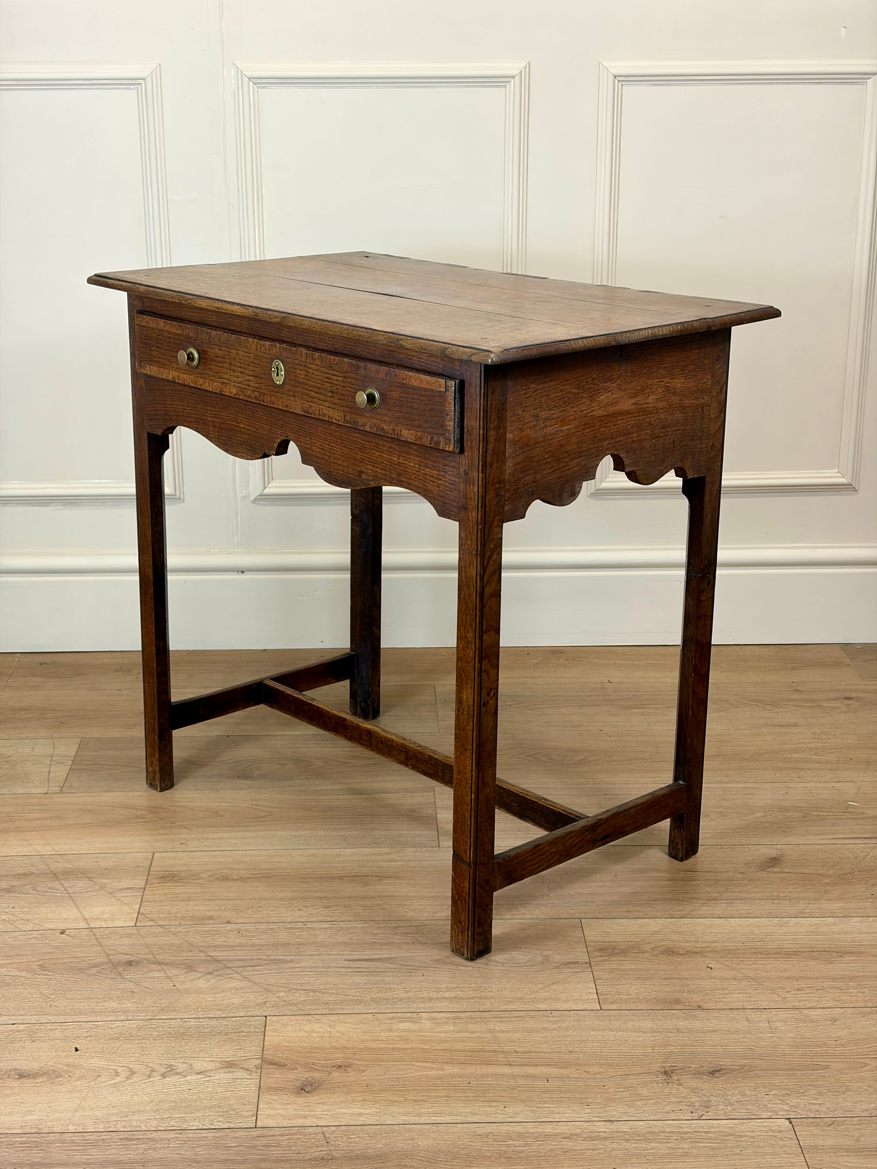 Wooden side table with a single drawer on a wooden floor against a white paneled wall.